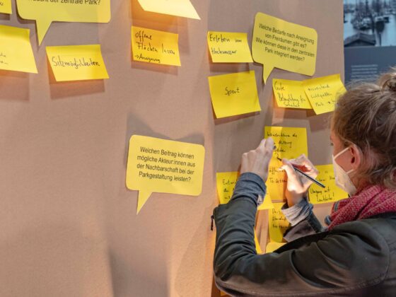 Frau beschriftet gelben Notizzettel an Stellwand