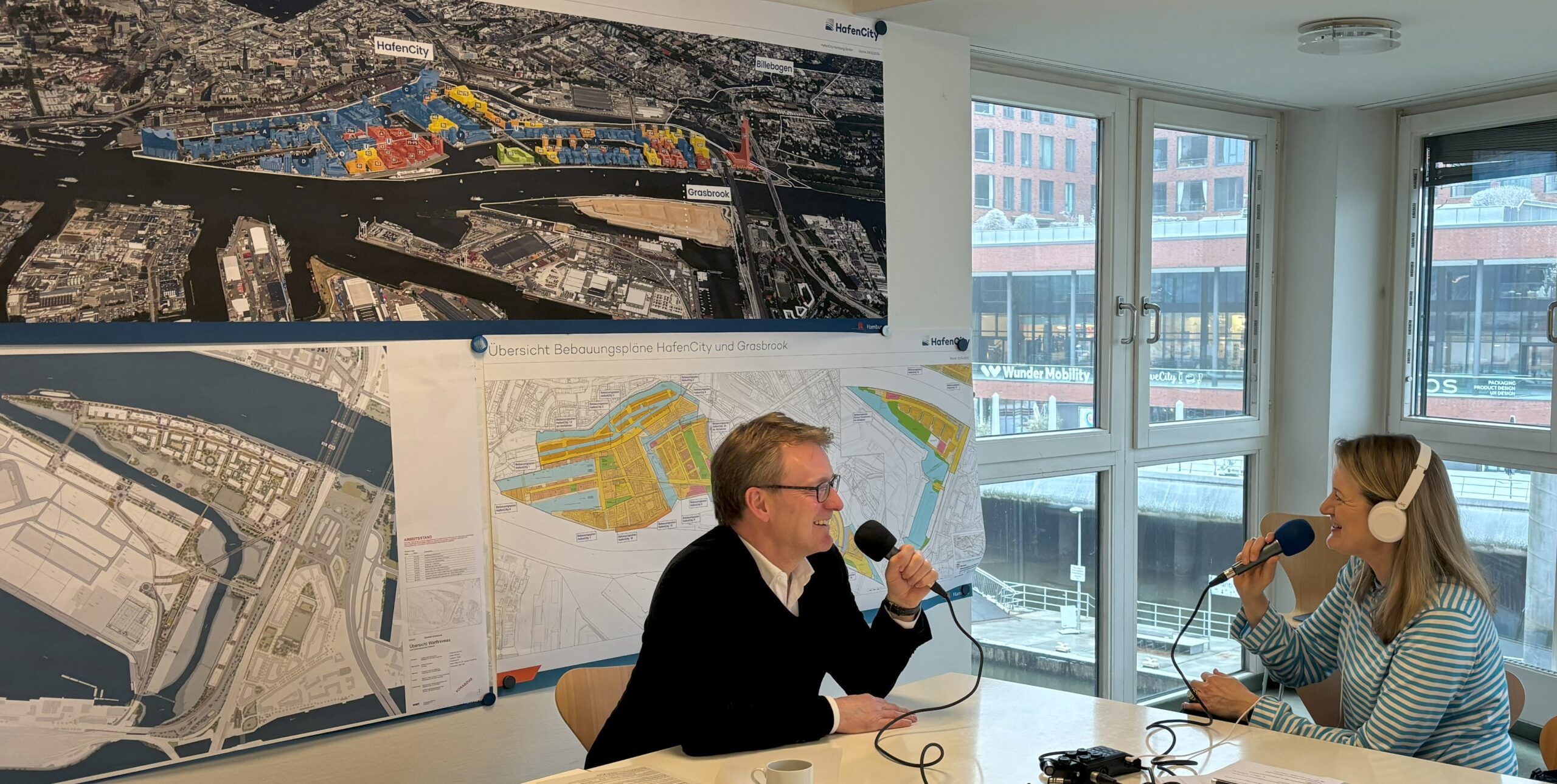 Zwei Personen bei der Aufnahme eines Podcasts, Karten im Hintergrund sichtbar